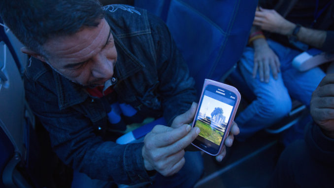 A Syrian refugee shows his home town of Hama on his phone while enroute to Canada. © IOM/Muse Mohammed 2015